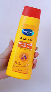 Person holding a yellow sunscreen bottle with red cap on a white background